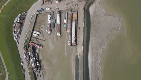 Aerial-birdeye-descending-over-marina-with-docked-ships-during-low-tide
