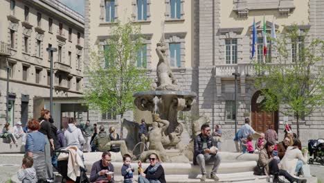 Gente-En-La-Piazza-Dante-Sentada-Junto-A-La-Fuente-Del-Tritón-En-Un-Día-Soleado-En-Bérgamo,-Italia