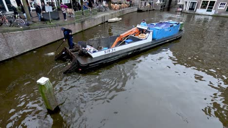 Cleaning-Crews-standing-on-a-barge-cleaning-rubbish,-trash-and-litter-from-a-canal-in-Amsterdam,-Netherlands