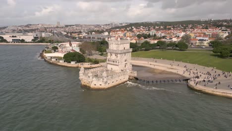 Rotierende-Luftaufnahme-Des-Atemberaubenden-Torre-De-Belém-Mit-Lissabon-Im-Hintergrund