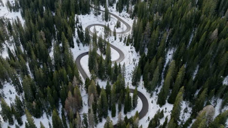 Aerial-View-Of-Winding-Road-Through-Snow-Covered-Giau-Pass-Surrounded-By-Alpine-Forest