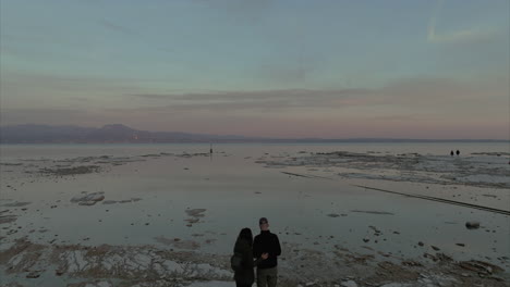 Luftaufnahme-Des-Gardasees-Bei-Sonnenuntergang-Mit-Dolly-Rückaufnahme-über-Einem-Am-Ufer-Stehenden-Paar