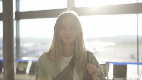 Portrait-of-a-stylish-young-blonde-girl-traveller-stands-in-airport-terminal-in-sunlight