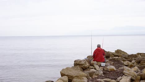 Ein-Fischmann-Sitzt-Auf-Einem-Felsen-Und-Blickt-Auf-Das-Meer