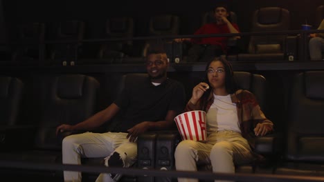 Gemischtrassiges-Junges-Paar-Sitzt-Im-Kino,-Schaut-Sich-Einen-Film-An-Und-Trinkt-Popcorn