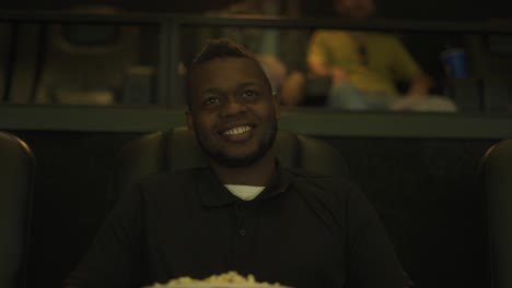 Afroamerikanischer-Mann-Sitzt-Im-Sessel-Und-Schaut-Sich-Eine-Komödie-Im-Kino-An,-Während-Er-Popcorn-Nimmt