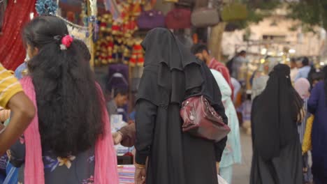 Indian-women-wearing-traditional-hijab,-burka-and-fully-covered-walking-through-the-market-outside-Charminar-for-shopping,-slow-motion-shot