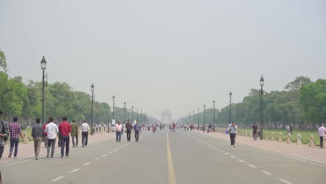 People-walking-down-the-street-of-Kartavya-Path-viewing-India-Gate-in-poor-air-quality,-low-visibility,-grey-smog,-foggy-mist-sky