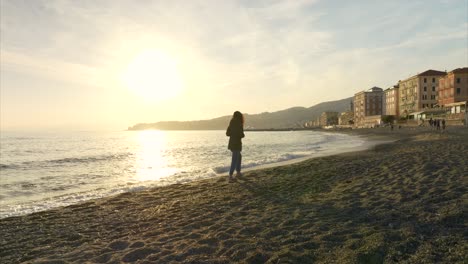 Silhouette-of-young-woman-walks-at-sunset-along-shore-of-Varazze-waterfront-beach-in-Liguria,-Italy
