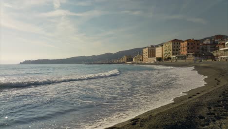 Varazze-beach-and-waves-breaking-on-shore-in-winter-season-with-cityscape-and-promenade-in-background,-Italy