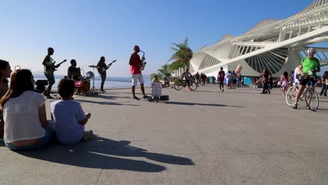 Menschen-Auf-Fahrrädern,-Menschen,-Die-Straßenmusikanten-Beobachten,-Und-Menschen,-Die-Bei-Sonnenuntergang-In-Praca-Maua-Im-Zentrum-Von-Rio-De-Janeiro,-Brasilien,-Herumlaufen