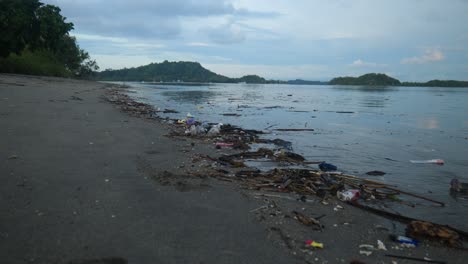 Slow-motion-wide-shot-of-rubbish-on-the-ocean-shore-with-islands-in-the-background-in-Lombok,-Indonesia