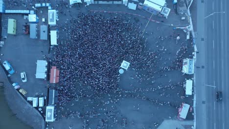 aerial-fly-down-into-the-crowds-birds-top-view-overlooking-the-stage-a-dolly-roll-reveal-of-the-big-screen-tv-as-white-giant-beach-ball-gets-tossed-around-light-traffic-blue-transit-bus-drives-over