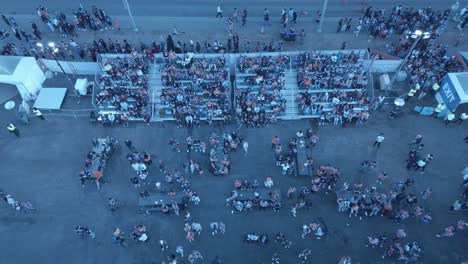 Aerial-drone-hold-overlooking-crowds-of-people-cheering-waving-at-camera-on-bleachers-outside-free-watch-party-next-to-Rogers-Place-arena-at-Oilers-away-game-in-Edmonton-as-angry-fans-await-to-get-in