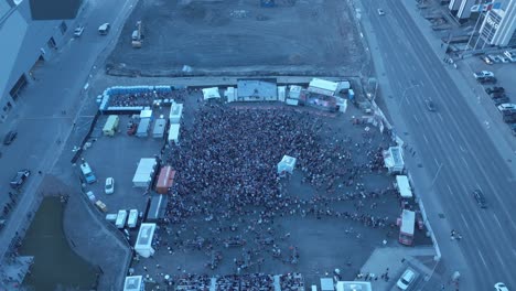 Barrier-fan-party-drone-fly-over-cheering-fans-at-mega-portable-tv-screen-with-food-truck-and-porta-potty-line-ups-crowds-outside-fencing-pushing-to-get-in-at-an-over-capacity-gathering-Oilers-fans
