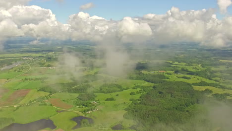 Aerial---Flying-through-clouds-over-green-landscape-on-sunny-day