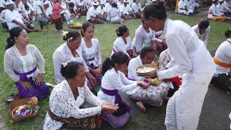 Eine-Ganz-In-Weiß-Gekleidete-Priesterin-Segnet-Mit-Weihwasser-Balinesische-Hinduistische-Gläubige-Bei-Einer-Religiösen-Tempelzeremonie-Auf-Bali,-Indonesien