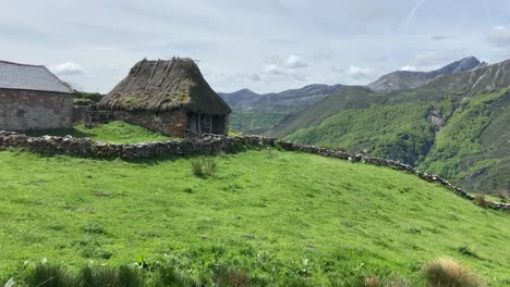 Panning-right-revealing-a-traditional-thatched-roof-cabin-in-middle-of-spectacular-green-valley-in-Asturias,-Spain