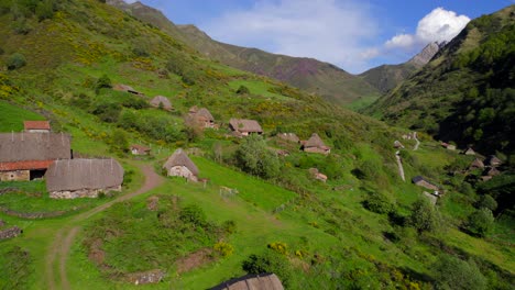 Aerial-ascent-over-idyllic-rural-thatched-roof-hut-village-in-green-valley-of-Asturias,-Spain