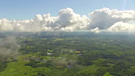 Aerial--POV-of-white-clouds-across-blue-sky-over-lush-green-landscape