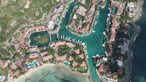 Stunning-Bird's-Eye-View-of-a-Marina-Featuring-Yachts,-Holiday-Condominiums,-and-a-Serene-Sea-with-Shadows-of-Passing-Clouds
