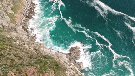 A-drone-captures-an-aerial-view-of-a-rocky-coastline,-with-waves-crashing-against-the-sharp-rocks