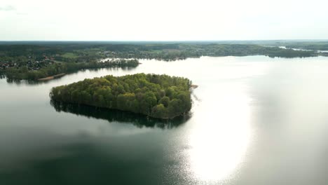 Una-Isla-Verde-En-Un-Lago,-Con-Muchos-árboles-Verdes-Y-El-Continente-Visible-Al-Fondo
