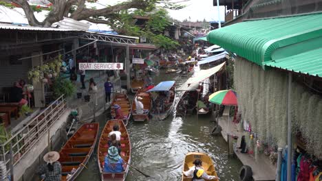 Vendors-operate-businesses-using-rowing-boats-to-navigate-the-narrow-canals-in-the-vibrant-Damnoen-Saduak-Floating-Market,-Ratchaburi-province,-South-West-of-Bangkok,-Thailand