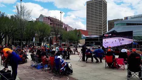 Free-Outdoor-Family-Friendly-Stanley-Cup-Playoffs-Game-at-Edmonton-City-Hall-people-seated-and-at-the-2nd-goal-standup-cheering-with-foil-orange-pom-poms-in-positive-loud-howls-of-happiness-B1-2