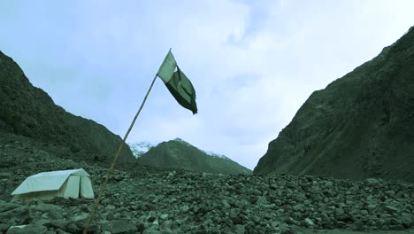 Torn-flag-of-Pakistan-going-down,-falpping-through-winds-in-the-middle-of-mountains