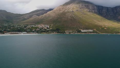 A-drone-captures-a-stunning-aerial-view-of-a-small-ocean-town-nestled-at-the-foot-of-cloudy-hills