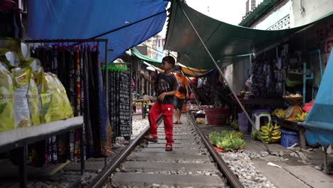 Menschen-Laufen-Auf-Der-Eisenbahnstrecke-Auf-Dem-Maeklong-Eisenbahnmarkt,-Der-Als-„Umbrella-Pulldown“-Markt-Bekannt-Ist-Und-Eine-Einzigartige-Und-Faszinierende-Attraktion-In-Der-Provinz-Samut-Songkhram-Im-Südwesten-Von-Bangkok,-Thailand,-Darstellt