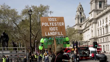 4-May-2023---Man-Protesting-Against-Plastics-Use-With-Green-Bottles-Hanging-From-Placard-In-Westminster