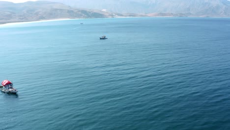 Un-Día-Soleado-En-La-Isla-De-Socotra-En-Yemen,-Con-Barcos-De-Pesca-Salpicando-Las-Olas-Del-Océano-Contra-Un-Impresionante-Telón-De-Fondo-De-Montaña