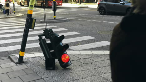 Damaged-broken-traffic-red-light-signal-on-the-streets-of-Stockholm,-with-commuters-walking-around