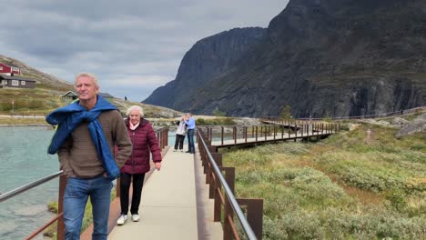 Couple-of-tourists-walking-over-the-platform-on-Trollstigen-close-to-the-water-and-with-houses-on-the-background-in-slow-motion