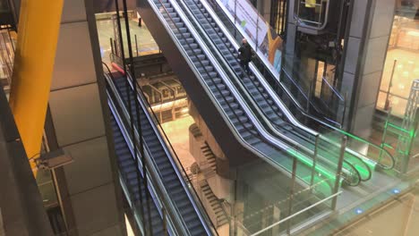 A-man-riding-an-escalator-in-a-modern-hall,-another-descending-with-an-elevator,-modern-construction-and-architectural-design,-metal-and-concrete-architecture