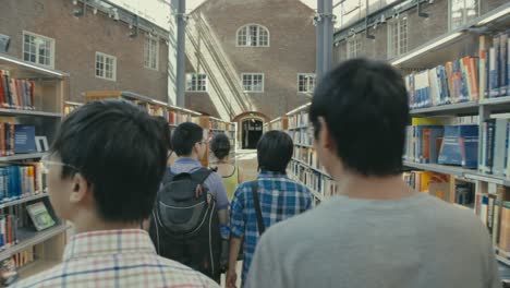 Eine-Gruppe-Chinesischer-Studenten-Geht-Durch-Reihen-Von-Bücherregalen-In-Der-Campusbibliothek