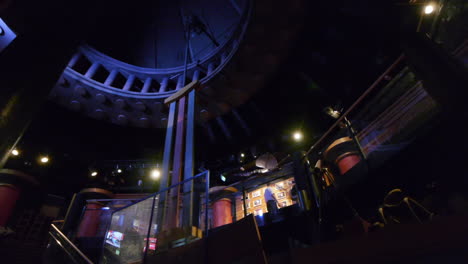 Looking-up-to-tourists-on-the-second-level-of-a-dark-museum-with-a-large-swinging-pendulum