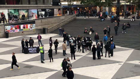 Manifestación-Anónima-De-Protesta-En-Una-Plaza-Comercial-De-Estocolmo,-Suecia,-Con-Gente-Caminando