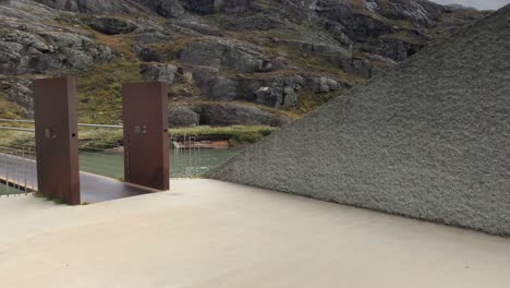Panning-shot-of-parking-lot-and-visitors-center-at-Trollstigen-in-Norway,-modern-architecture-in-natural-landscape,-concrete-and-iron-combined-to-blend-in-with-wild-rivers-and-surrounding-mountains