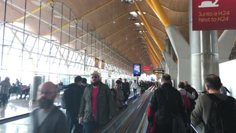 Menschen,-Die-Im-Modernen-Terminalbereich-Des-Internationalen-Flughafens-Madrid-Barajas-Auf-Einem-Express-Gehweg-In-Beide-Richtungen-Fahren,-Eine-Gruppe-Von-Passagieren,-Die-Vorbeikommen-Und-Auf-Einer-Flachen-Rolltreppe-Laufen