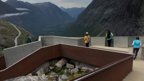 Tourists-walking-across-viewing-platforms-at-Trollstigen-in-Norway-and-waving-to-the-camera,-modern-architecture-in-natural-landscape,-concrete-and-steel-blending-with-nature,-mountains-in-background