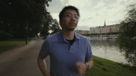 Close-up-of-young-man-with-glasses-jogging-beside-a-waterway-on-a-gravel-walking-path