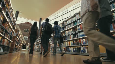 Eine-Gruppe-Chinesischer-Studenten-Geht-Durch-Reihen-Von-Bücherregalen-In-Der-Campusbibliothek,-Während-Ein-Fotograf-Ihnen-Folgt