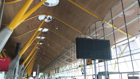 Airport-terminal-at-Madrid-Barajas-International-Airport,-slow-tilt-up-from-busy-building,-people-rushing,-revealing-the-unique-architecture-of-the-terminal,-with-wood-faced-ceiling-with-large-windows