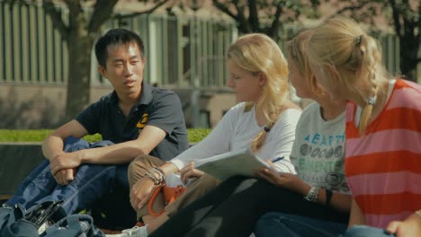 Close-up-view-of-pretty-blonde-women-talking-with-an-Asian-student-at-Chalmers-University-as-they-sit-outside-on-a-warm-day