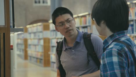 Chinesische-Studenten-Diskutieren-In-Der-Universitätsbibliothek,-Während-Sie-Bücher-Für-Ihre-Recherche-Auswählen