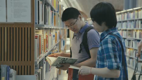 Dos-Jóvenes-Asiáticos-Seleccionan-Libros-De-Filas-De-Estanterías-En-La-Biblioteca-De-La-Universidad