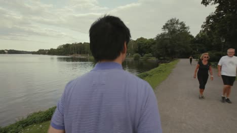 Close-up-of-a-young-Asian-man-in-a-purple-shirt-jogging-beside-a-pond-on-a-gravel-walking-path